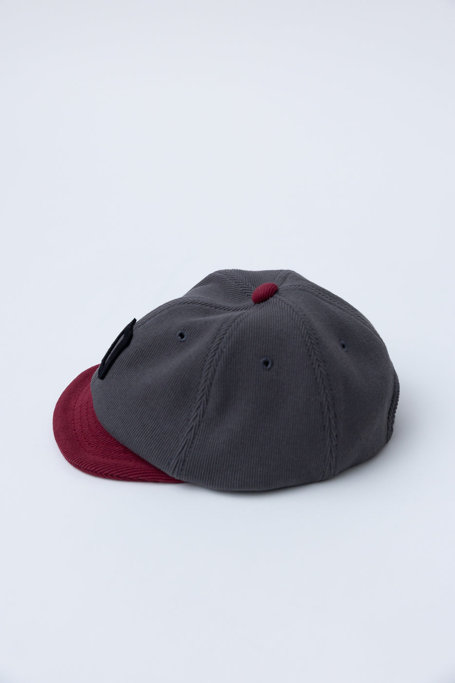 JM6310 - GG Rib BB Cap D - 318 Gray x Oxblood: A charcoal corduroy cap with a burgundy brim, crafted from repurposed cotton rib and sweatshirt scraps for sustainable comfort.