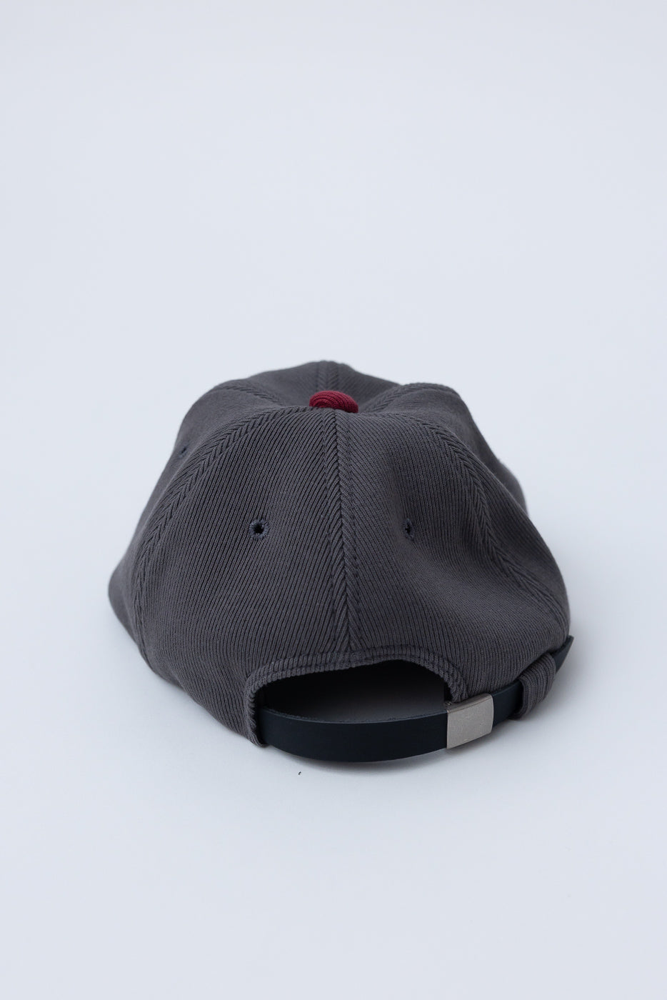 JM6310 - GG Rib BB Cap D - 318 Gray x Oxblood: Back view of a charcoal cap featuring red top button, adjustable strap with metal clasp, and ribbed fabric panels, highlighting its sustainable design.