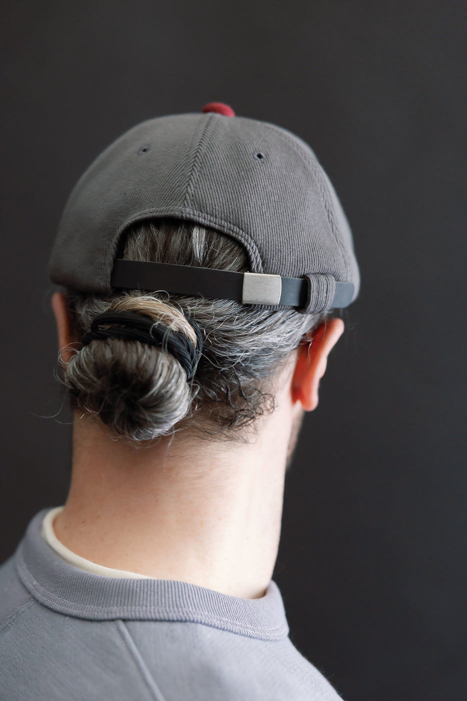 The JM6310 - GG Rib BB Cap D - 318 Gray x Oxblood is worn backward on a person's head, showcasing its stretchy, recycled cotton ribbed fabric and comfortable fit.