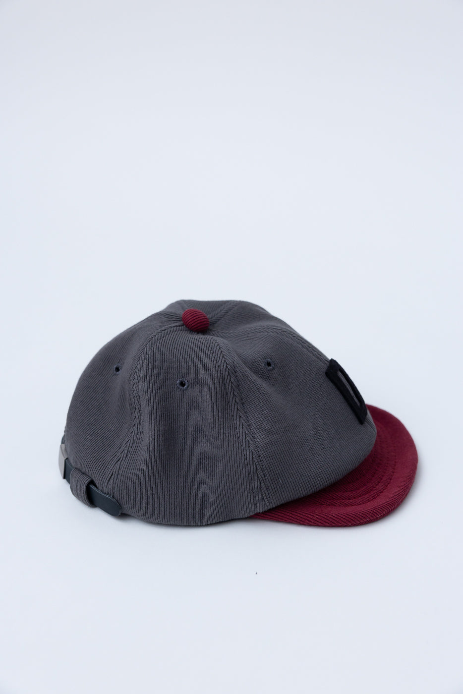 JM6310 - GG Rib BB Cap D - 318 Gray x Oxblood: A stylish, sustainable six-panel cap with a charcoal gray crown and maroon brim, made from recycled ribbed cotton fabric for comfort and adaptability.