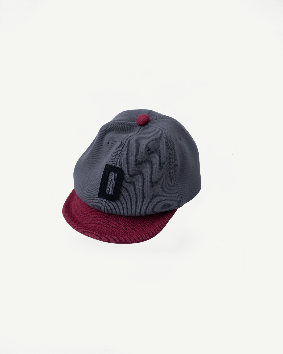 JM6310 GG Rib BB Cap D - 318 Gray x Oxblood features a slate gray crown and burgundy brim, with a logo patch on the front, made from repurposed cotton rib for comfort.