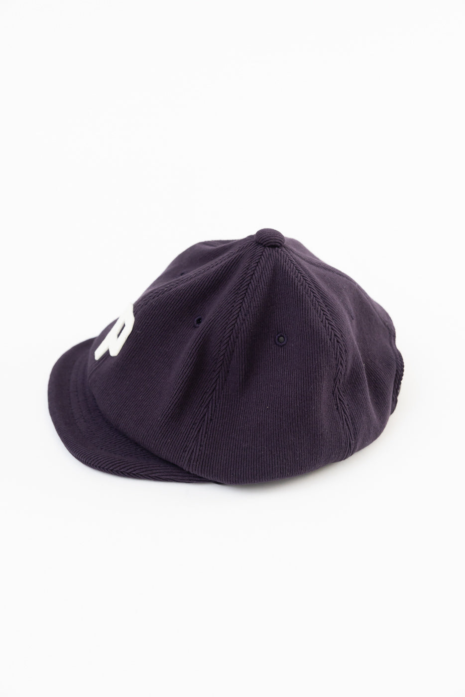 Side view of a dark purple corduroy baseball cap flat lay on white background.