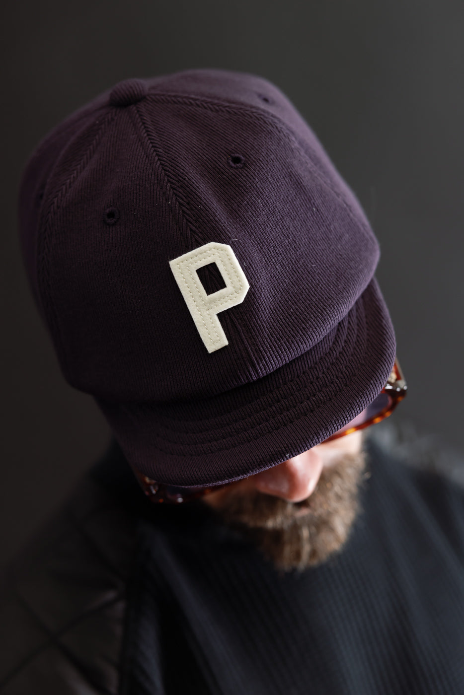Close-up front view of a dark purple corduroy baseball cap with a white letter P patch.