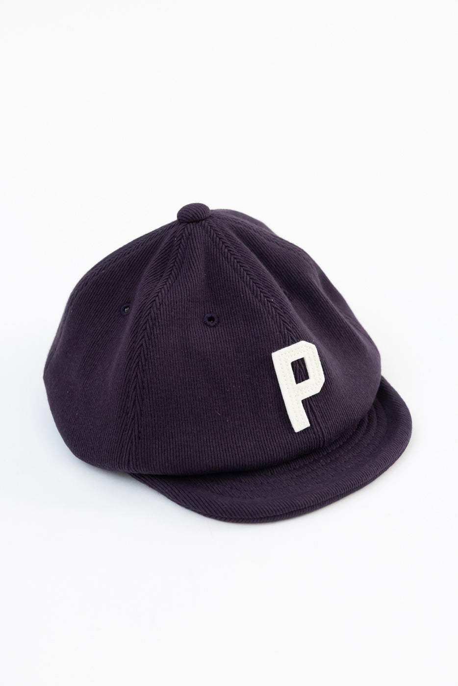 Close-up front view of a purple corduroy cap featuring a white 'P' embroidery.
