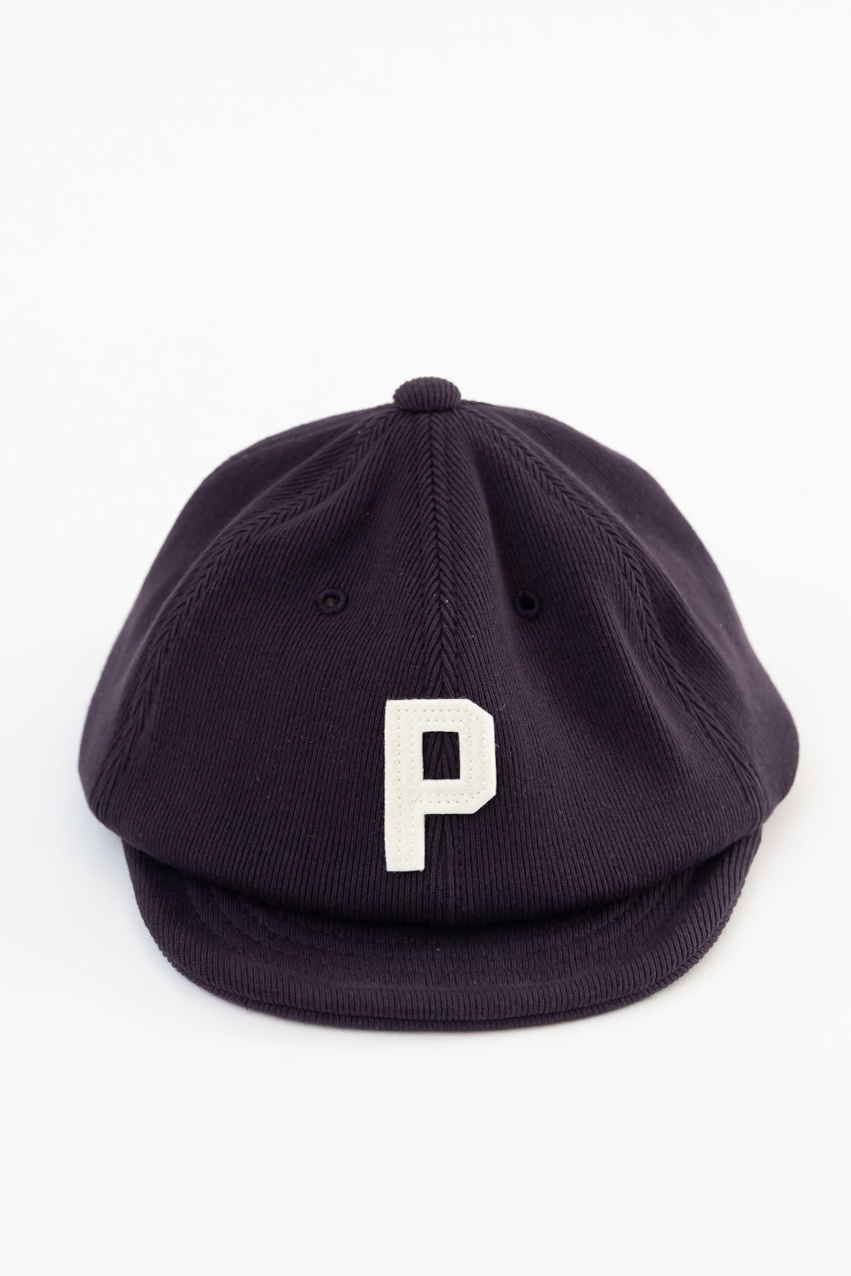 Front view flat lay of a navy corduroy newsboy cap featuring a white letter P patch.