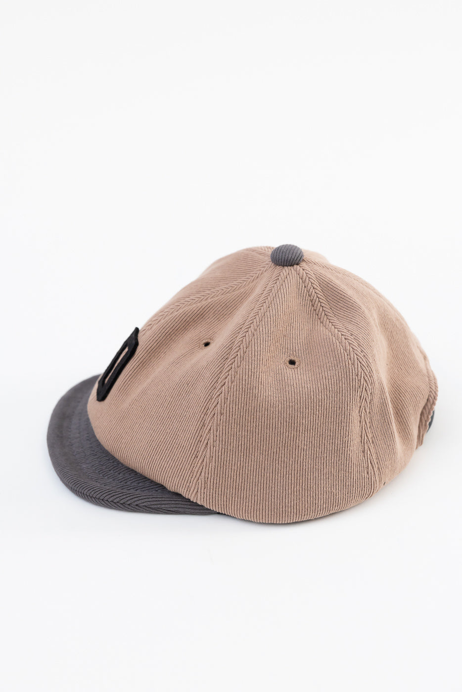 Close-up side view of a tan corduroy cap with a grey brim and button.