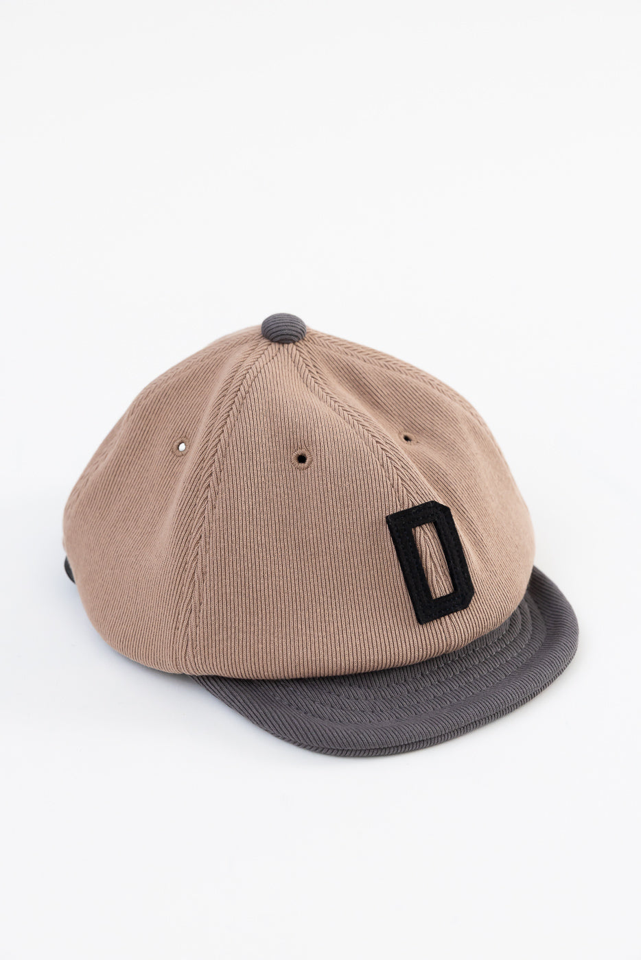 Front side view of a tan corduroy baseball cap with a black letter D patch and grey brim.