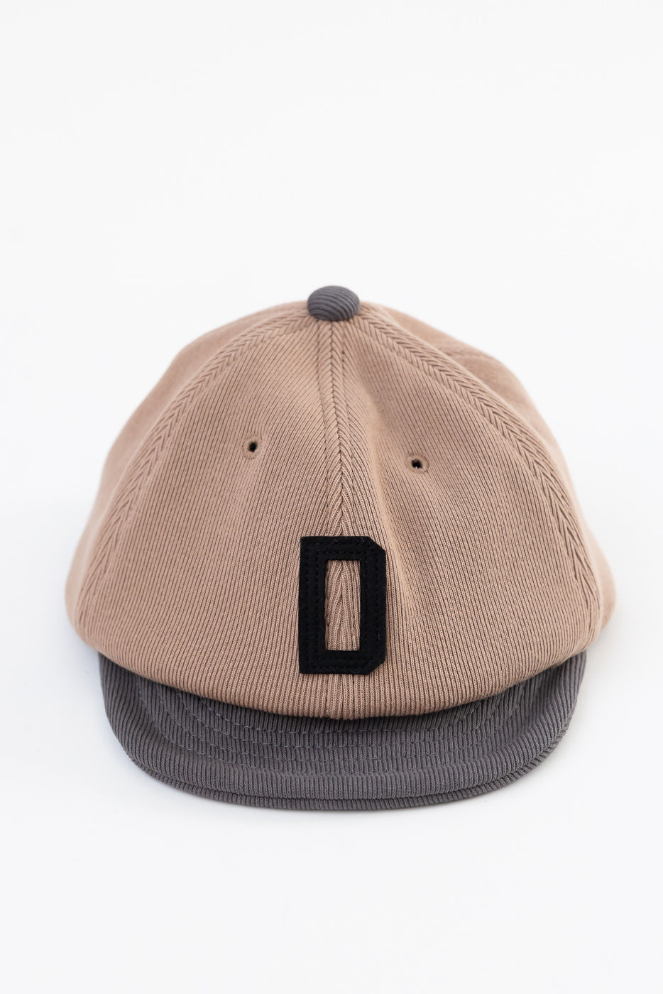 Front view flat lay of a tan corduroy baseball cap with a black letter D patch and grey brim.
