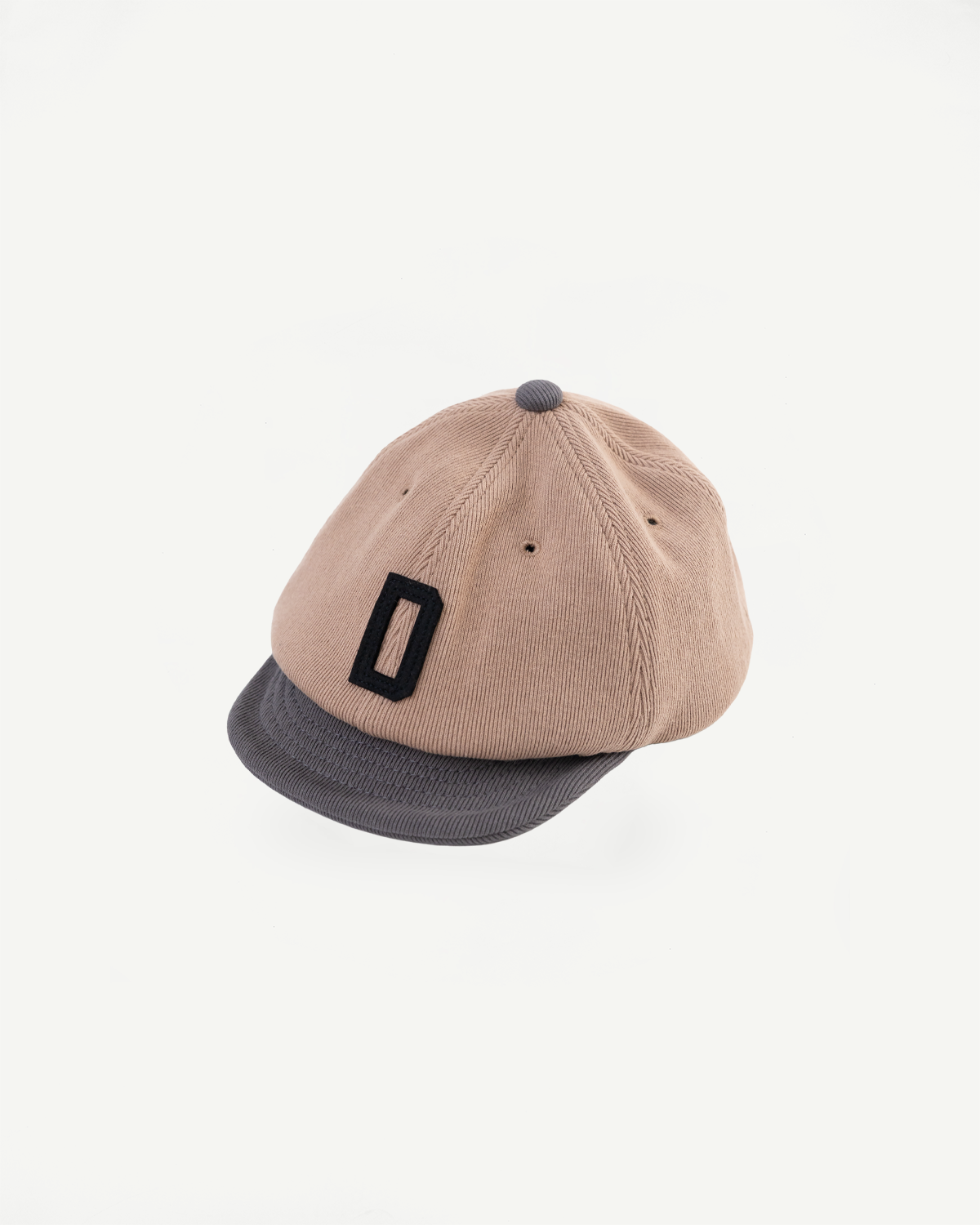 Front view of a tan corduroy baseball cap with a grey brim and black letter patch.
