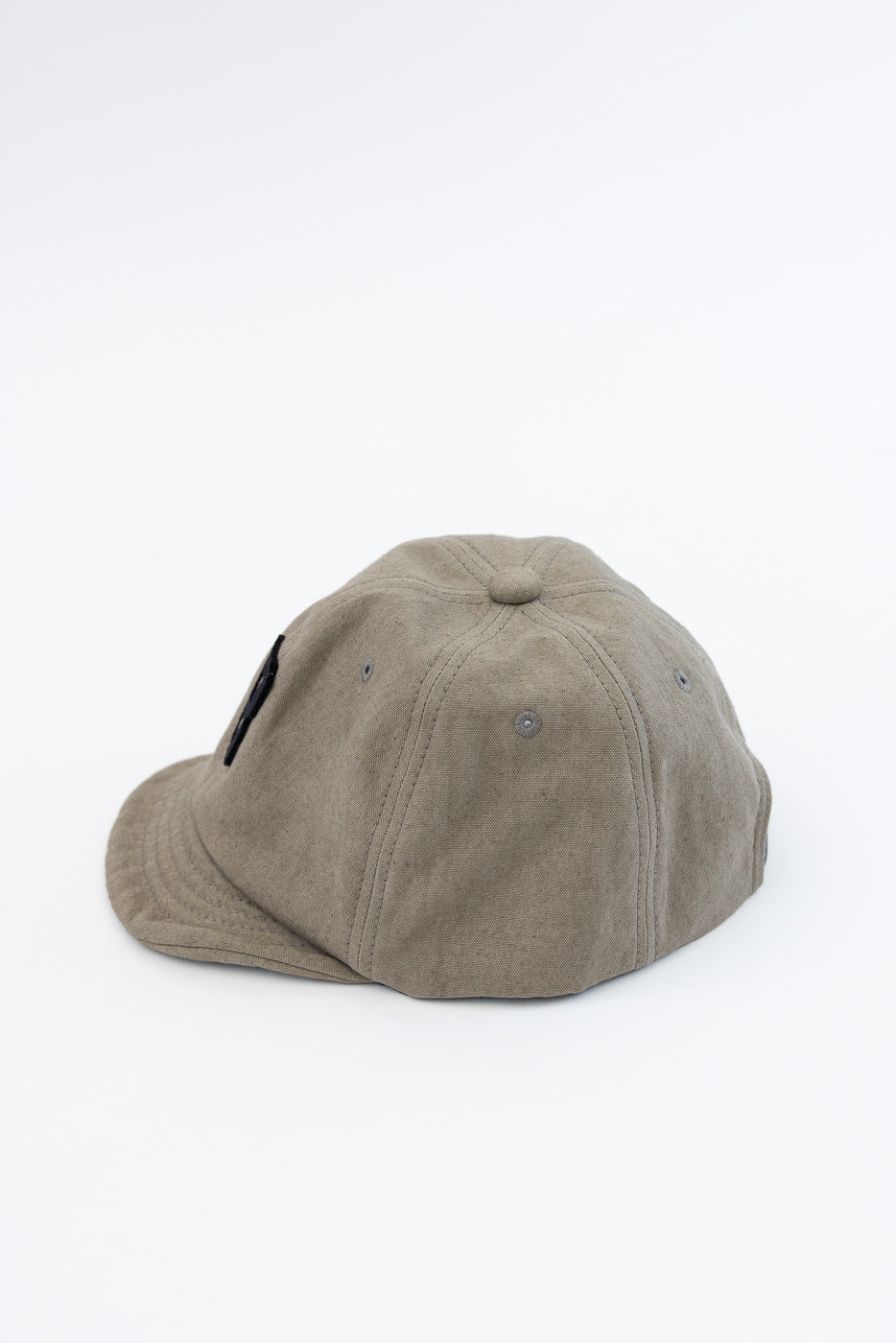Flat lay side view of olive cotton cap showing curved brim, panel stitching, and black tag detail