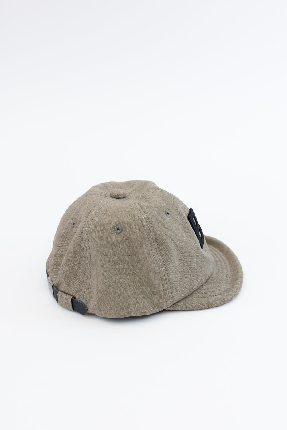 Tan baseball cap back view, showing adjustable strap, fabric texture, and black logo patch on side