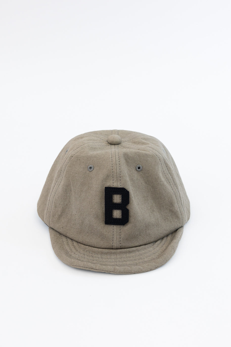Front view of beige cap with black 'B' patch, showing fabric texture and curved brim