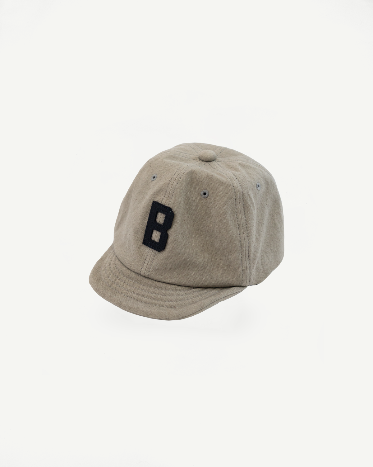 Tan baseball cap front view, black embroidered 'B' logo, structured panels, curved brim, fabric texture close-up