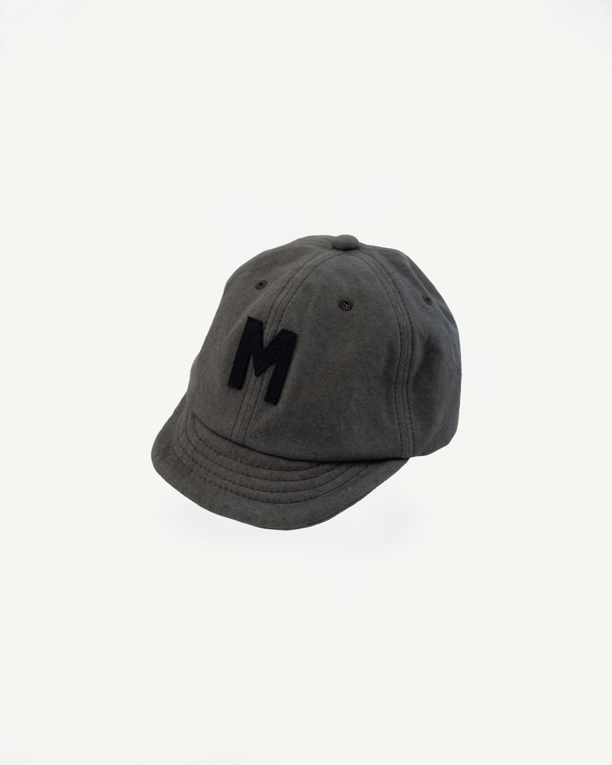 Front angled view of dark moss gray canvas baseball cap with black M patch, flat lay.