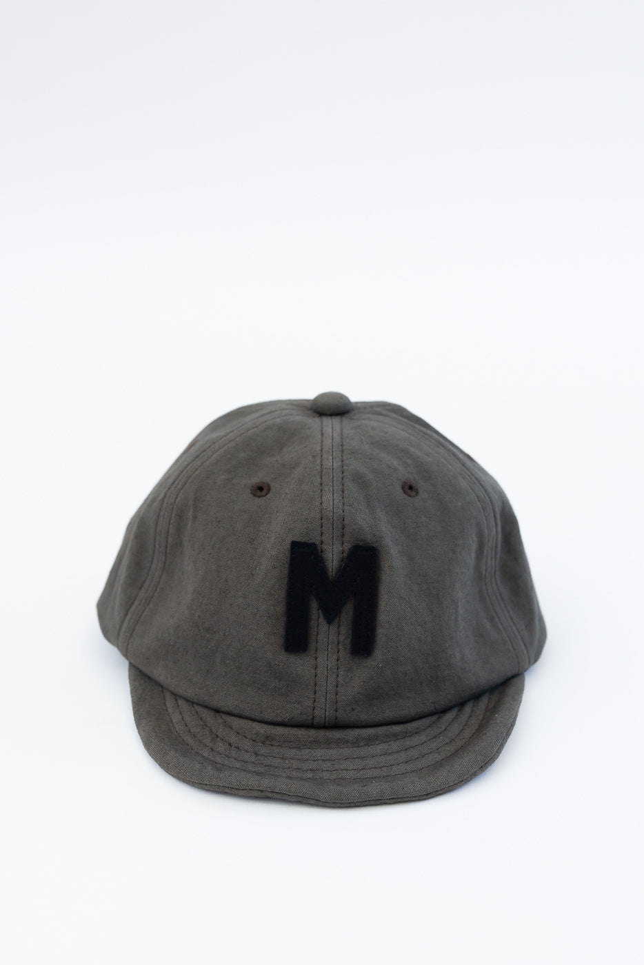 Front close-up of dark moss gray canvas baseball cap with black M patch and curved brim