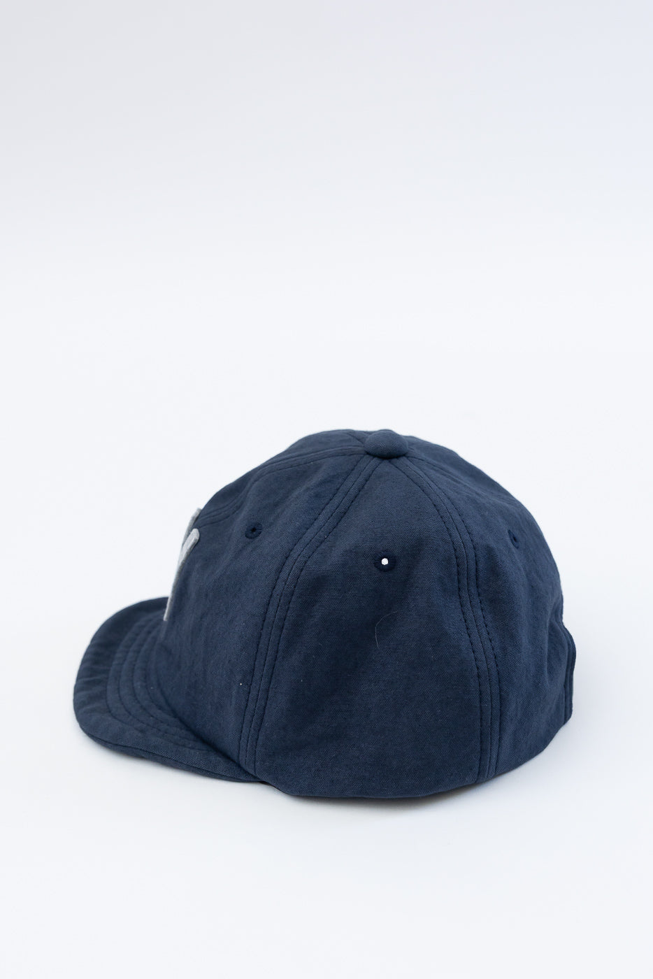 Close-up of navy canvas baseball cap, left-back side, showing seam stitching and button top.