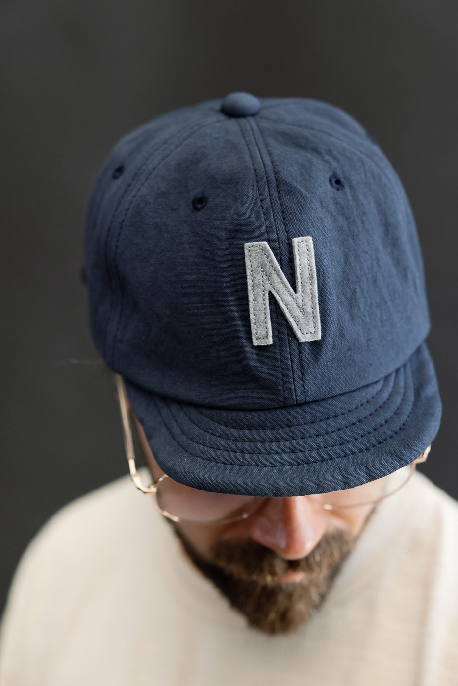 Close-up front view of navy canvas baseball cap with N patch, worn by male model, 5'9