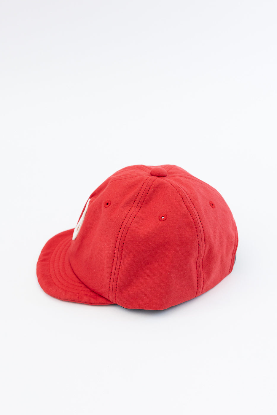 Red baseball cap, side view showing curved brim, stitched panels, and fabric texture on white background