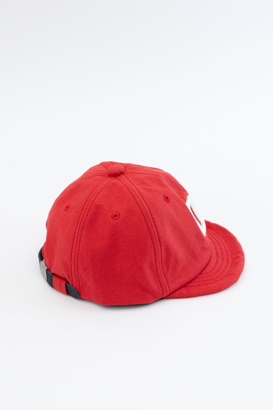Red baseball cap back view, showing adjustable strap, stitched panels, and white logo detail on side