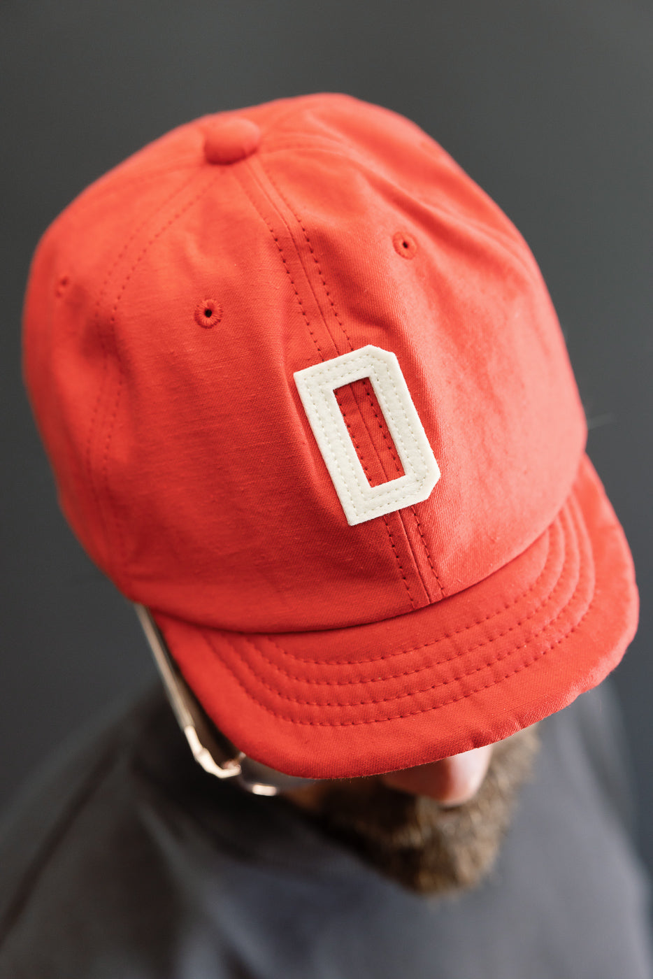 Close-up front view of red cap with white 'O' patch, worn by male model, showcasing fabric texture and stitching.