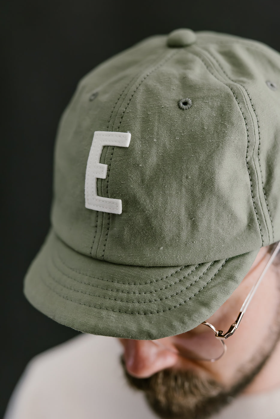 Green cap with a white 'E' logo worn by a person against a dark background