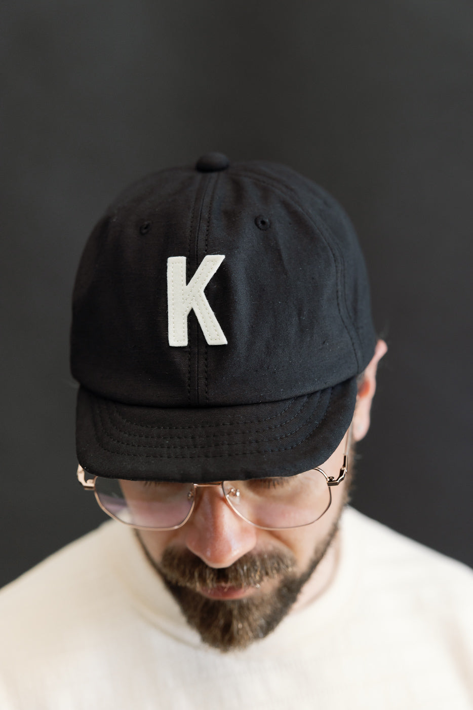 Close-up front view of black cap with white K patch, worn by male model 5'9