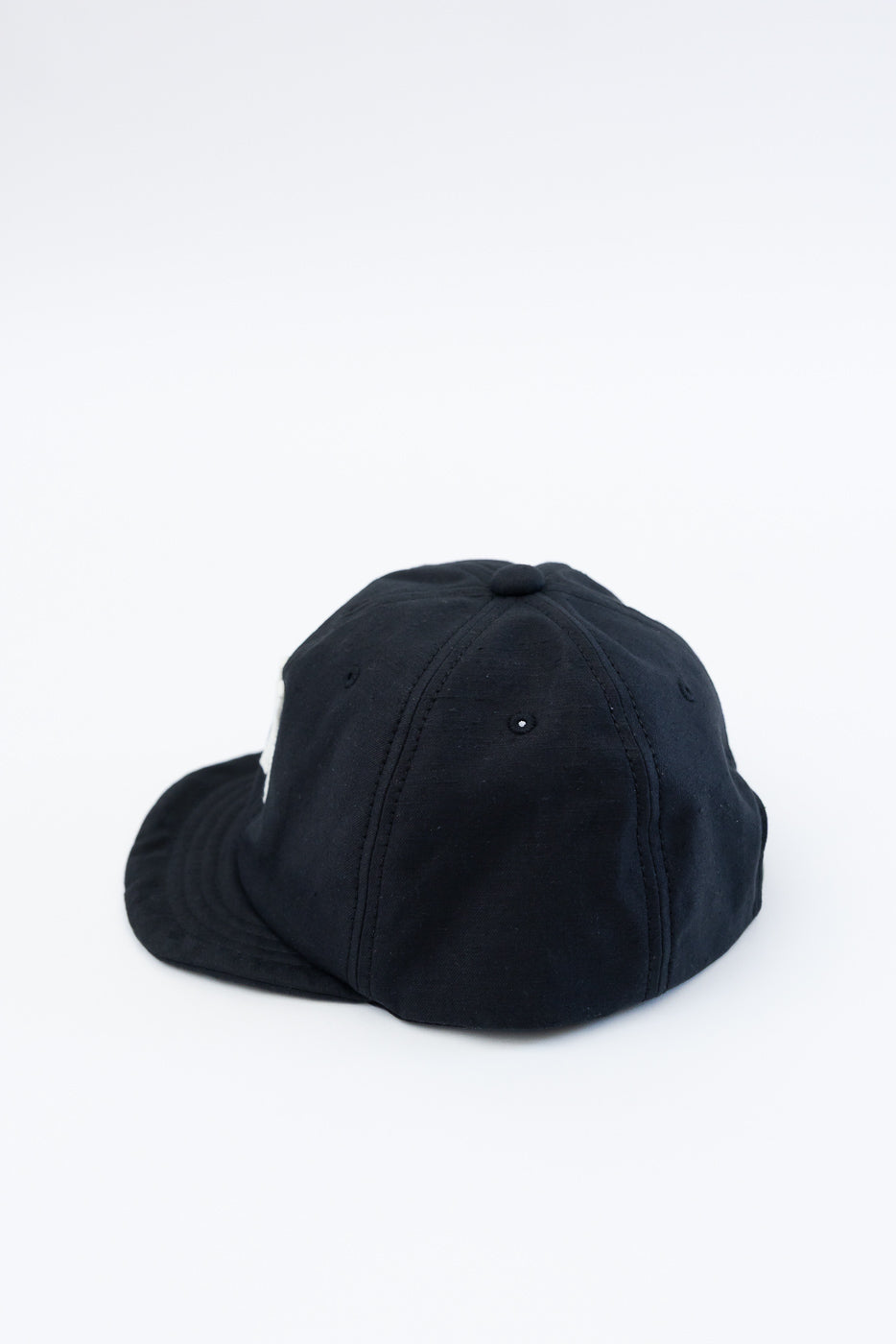 Back angled view of black baseball cap, close-up showing fabric texture and stitching details.