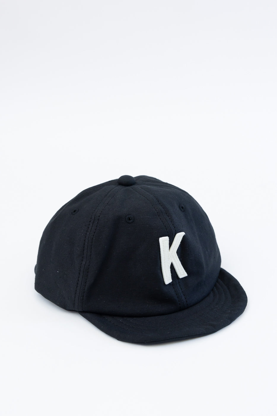 Close-up of front and side of black baseball cap with white letter K embroidery detail.