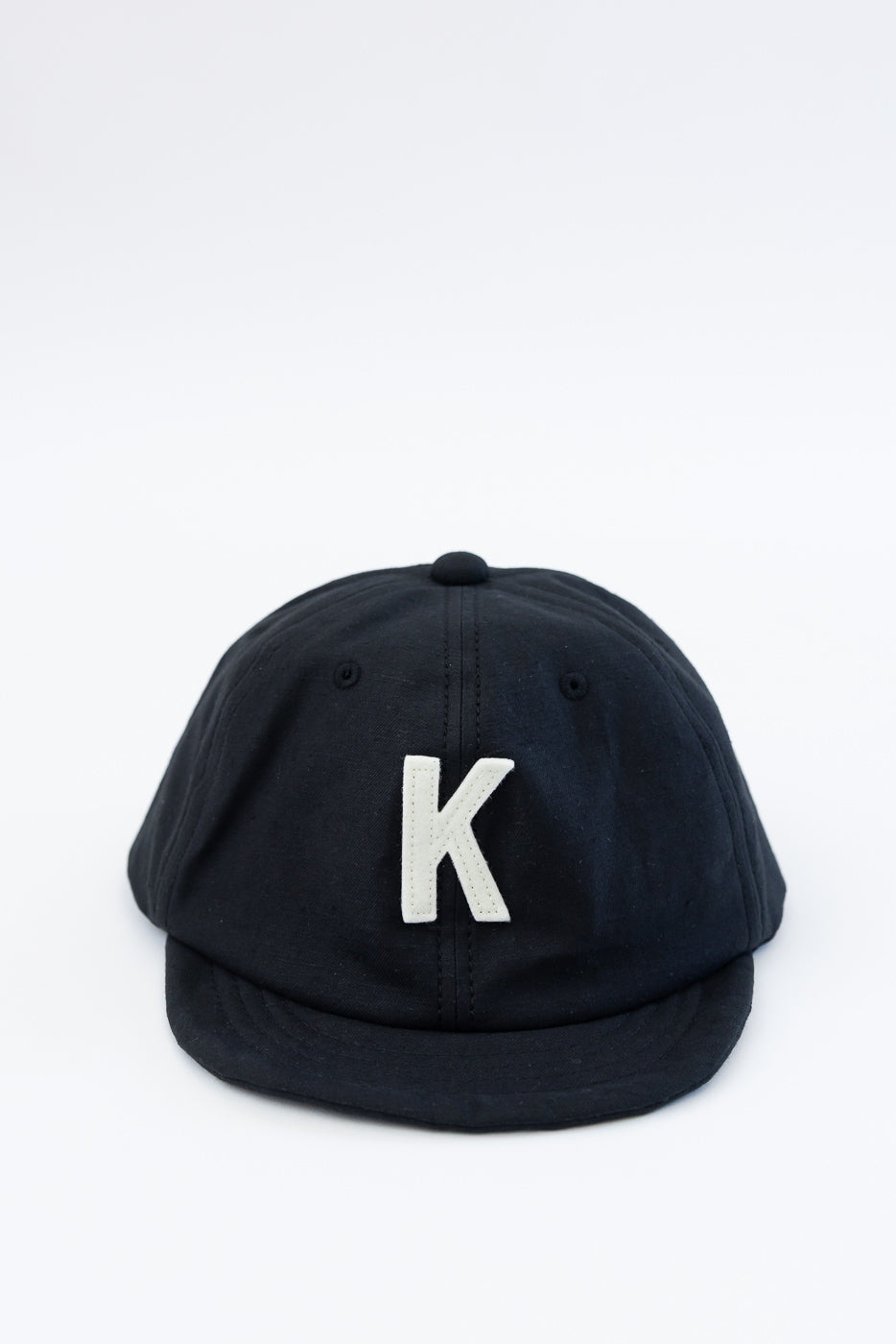 Front close-up of black baseball cap with white K patch and curved brim