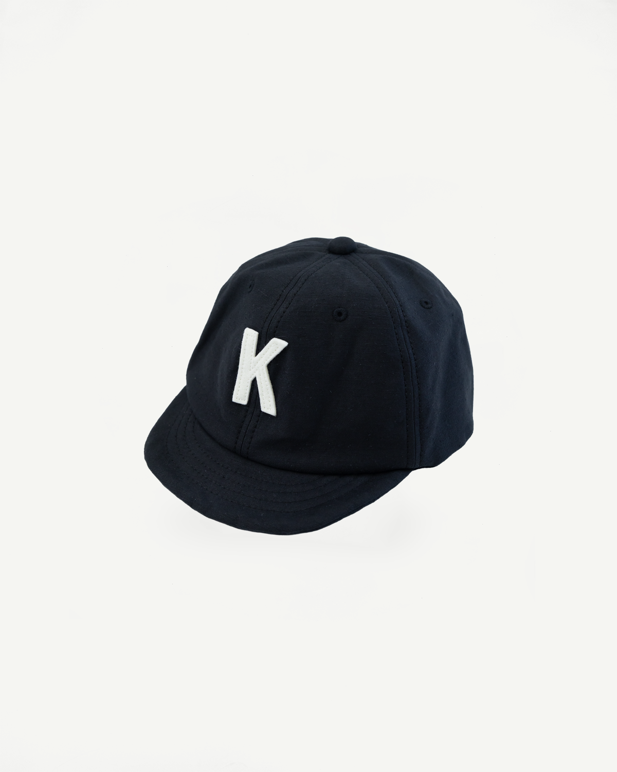 Close-up angled front view of black baseball cap with white embroidered K logo.