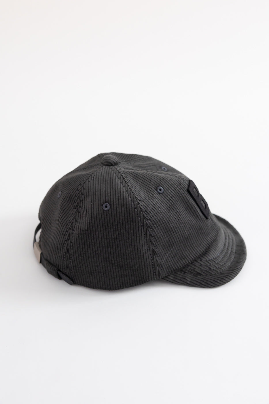 Fade black corduroy baseball cap flat lay, left-back side, textured fabric and eyelets visible