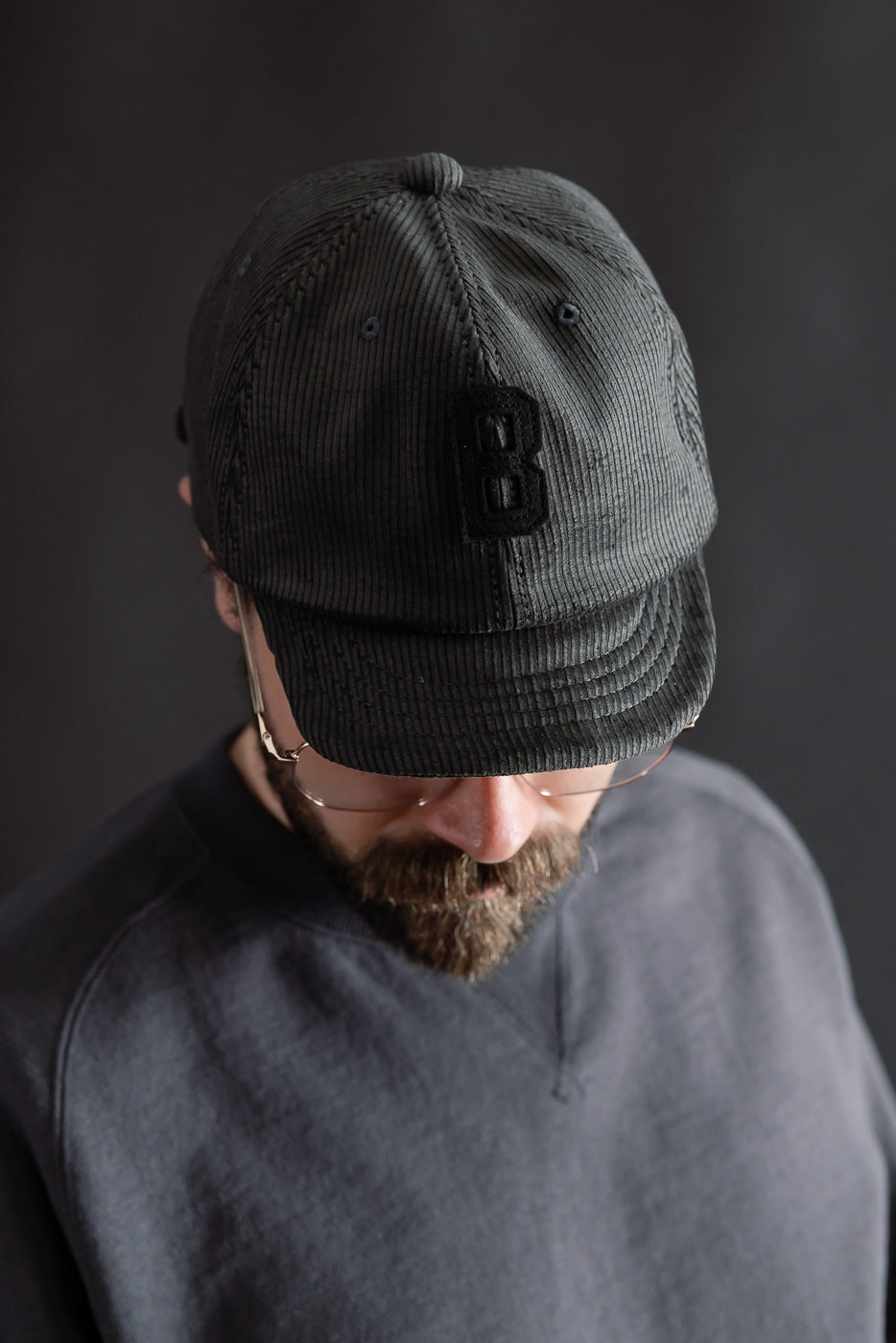 Close-up front view of fade black corduroy cap with B patch, worn by male model, 5'9