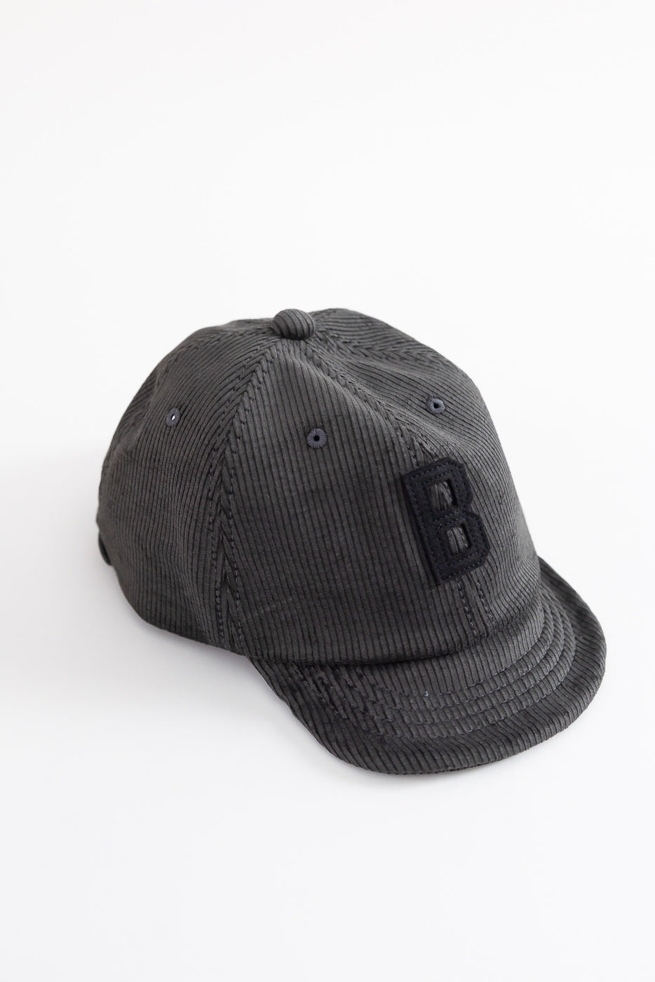 Close-up of black corduroy baseball cap, angled front view, textured fabric, raised B patch.