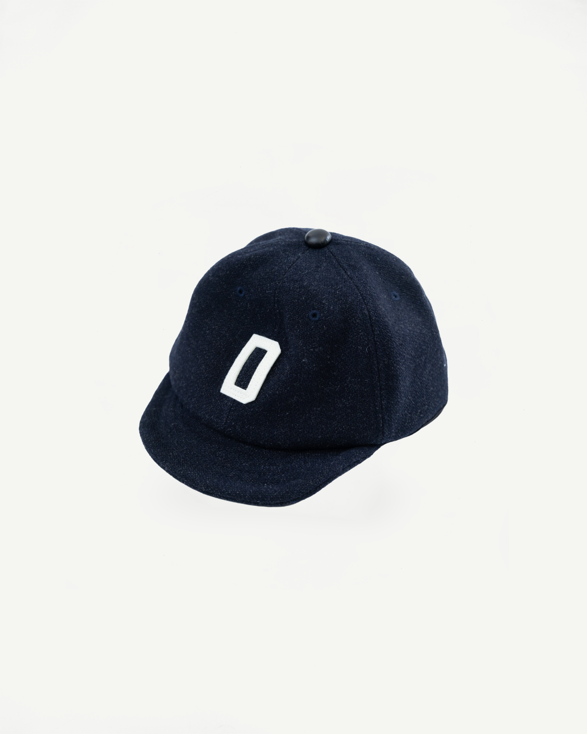 Flat lay front view of dark navy wool baseball cap with white embroidered letter and black top button