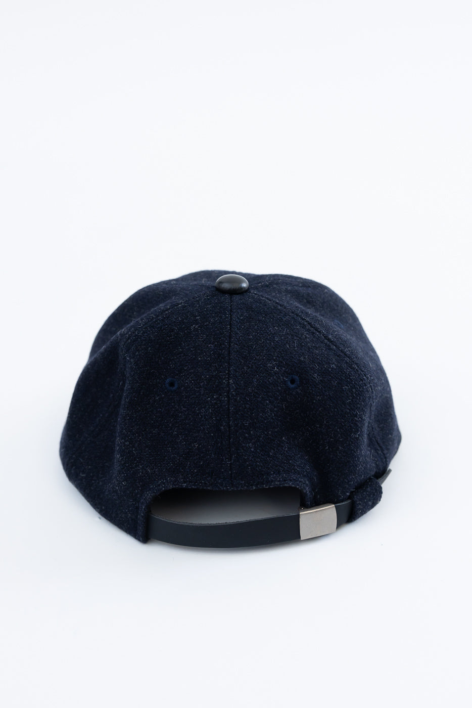 Close-up rear view of dark navy wool baseball cap, showing adjustable strap and button top.