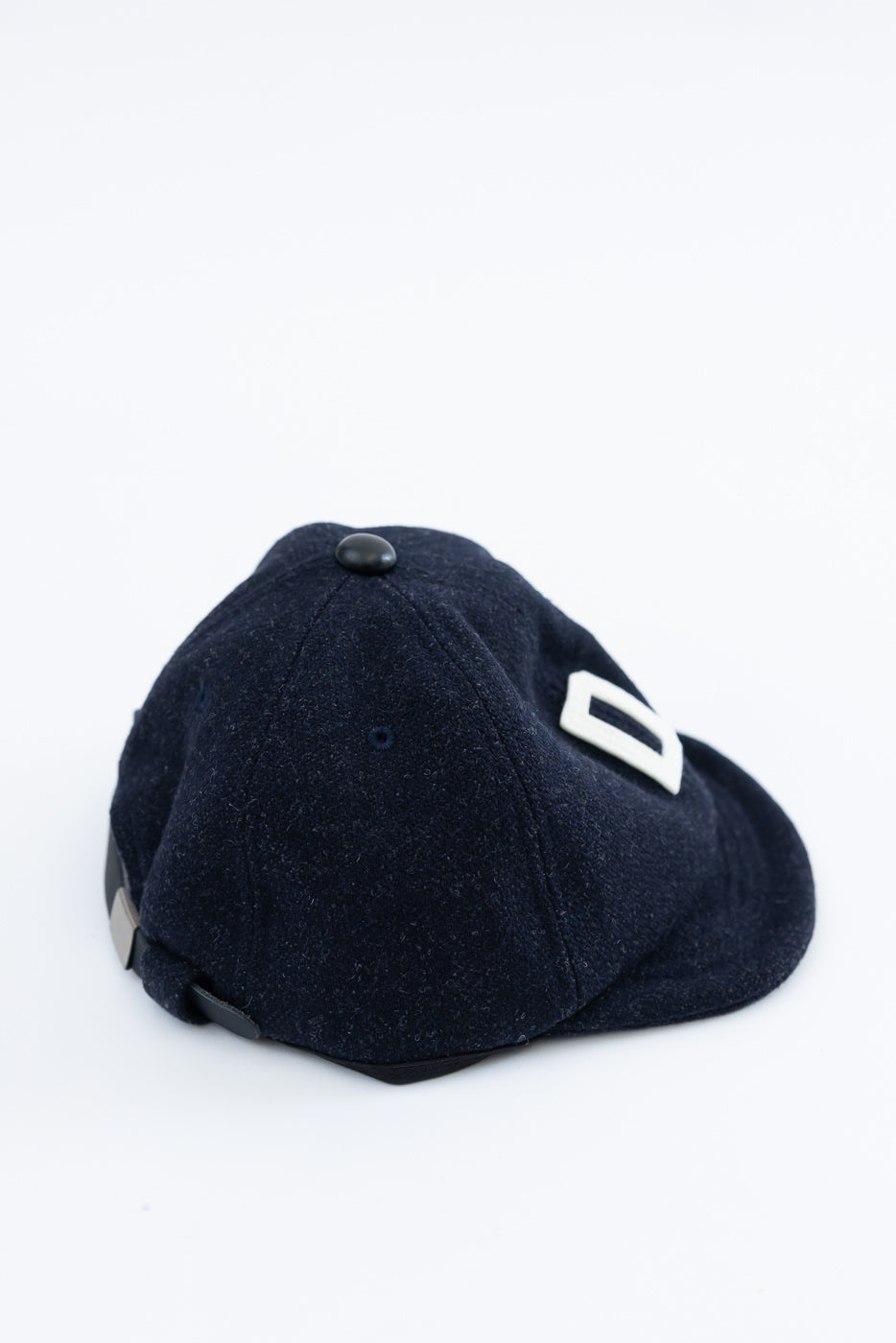 Close-up of dark navy melton wool baseball cap, rear and side view showing textured fabric and button top.