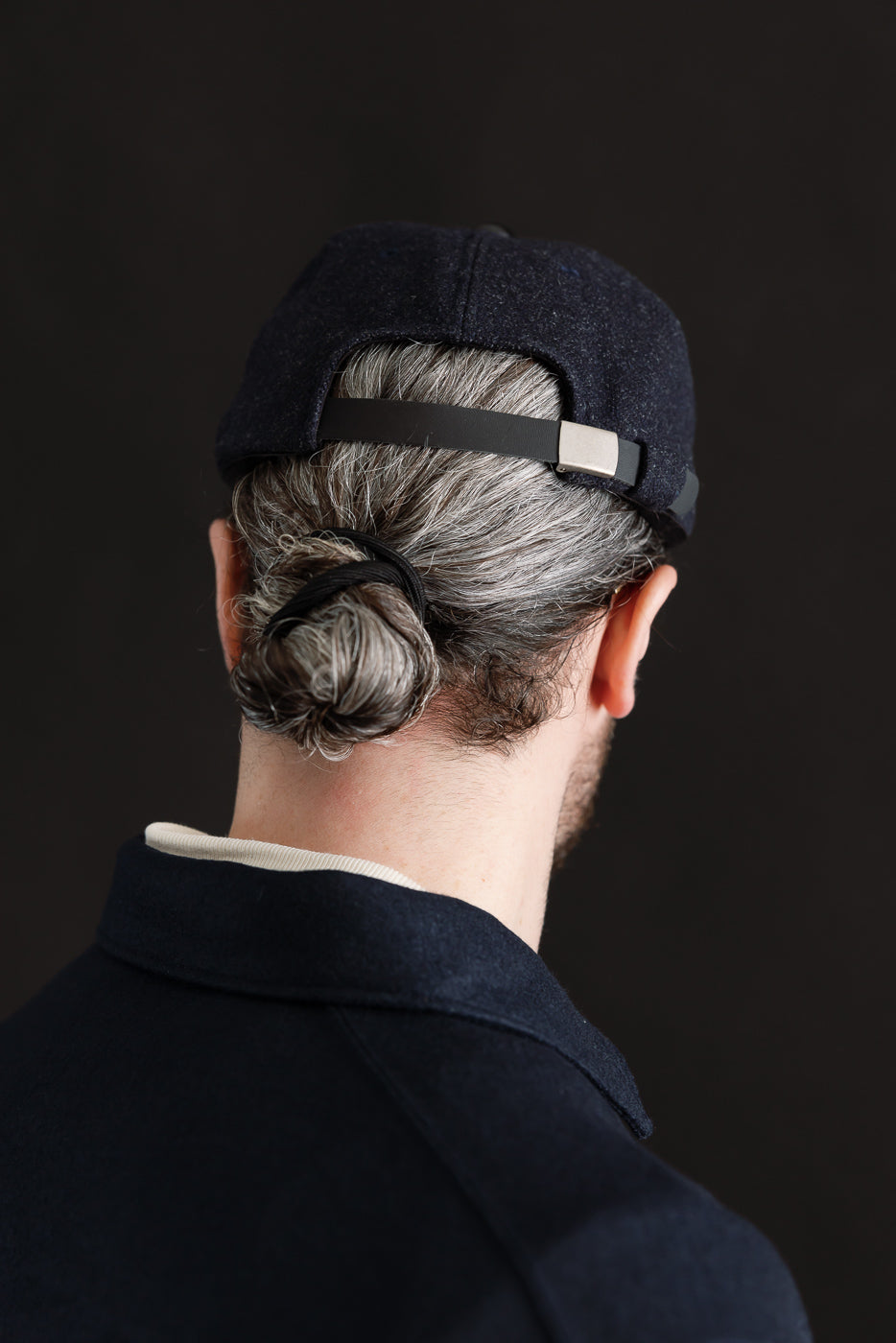 Close-up of back of dark navy wool cap with leather strap, worn by male model, 5'9