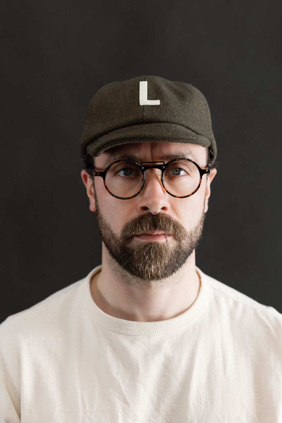 Front close-up of olive green wool baseball cap with white L, worn by male model 5'9