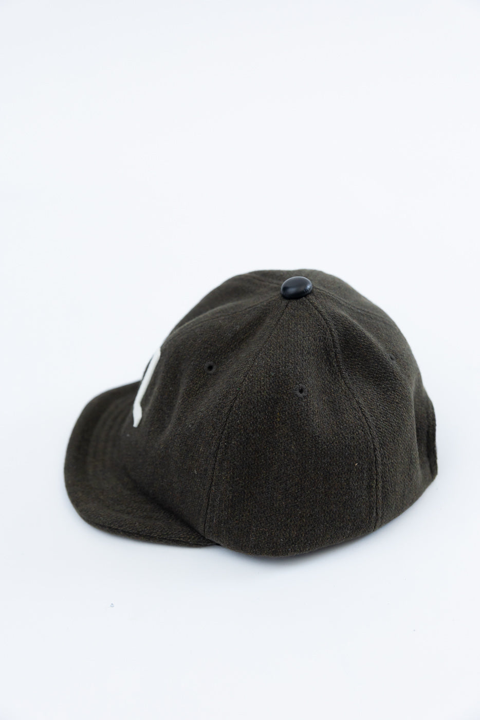 Close-up of the back and side of a dark green wool baseball cap showing fabric texture and top button.
