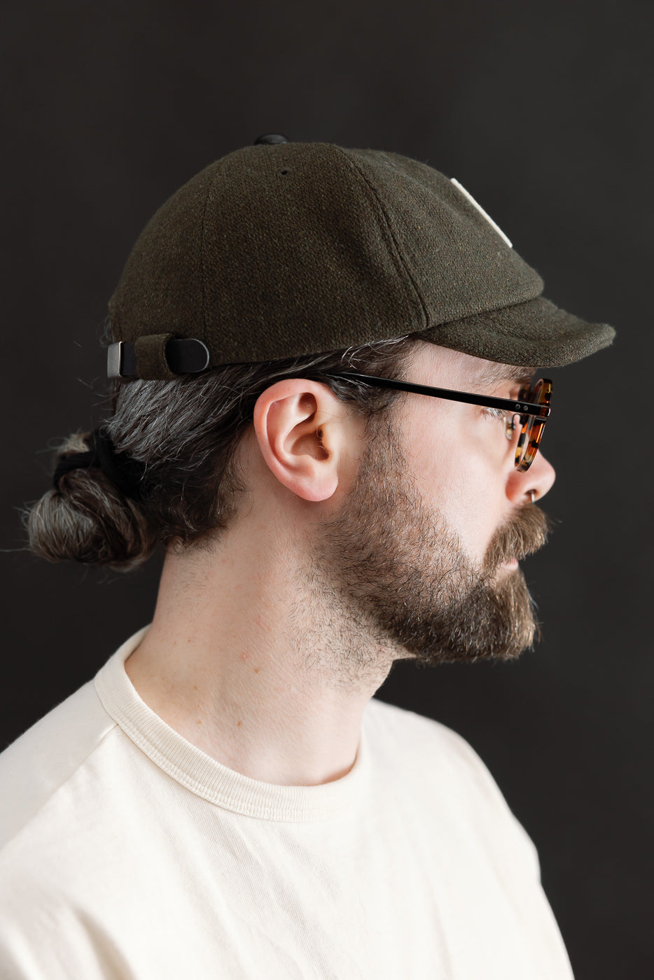 Close-up side view of men's loden green Melton baseball cap with adjustable strap on male model, 5'9