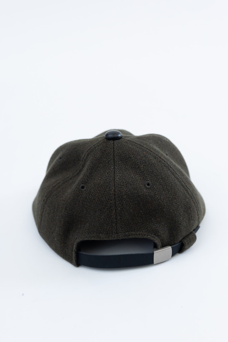 Close-up of the back of a loden green melton wool cap with black adjustable strap and metal clasp.