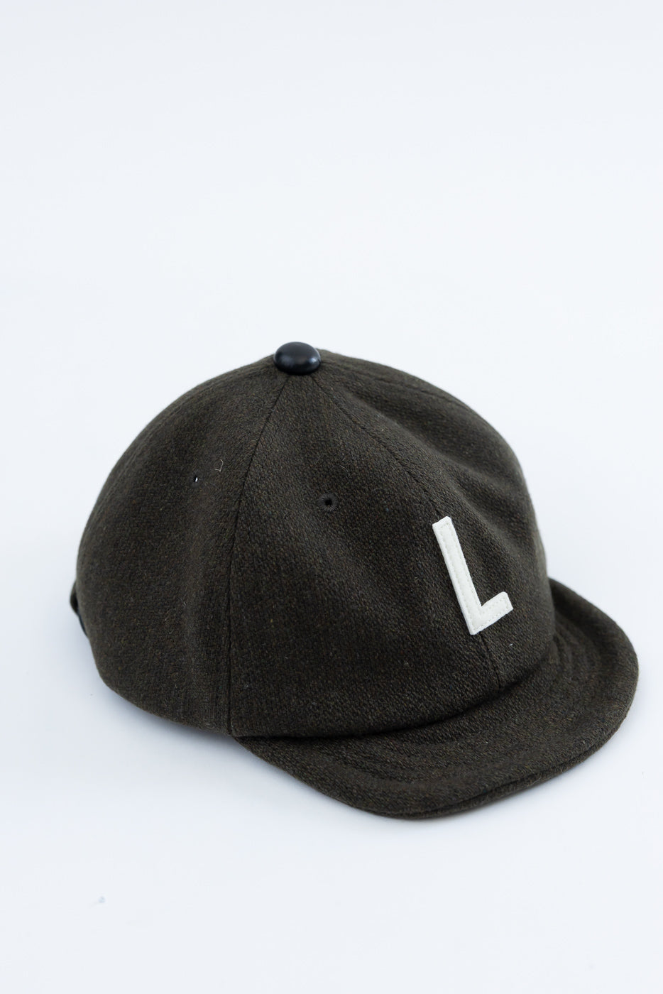 Close-up angled front view of olive green wool baseball cap with white 'L' applique.