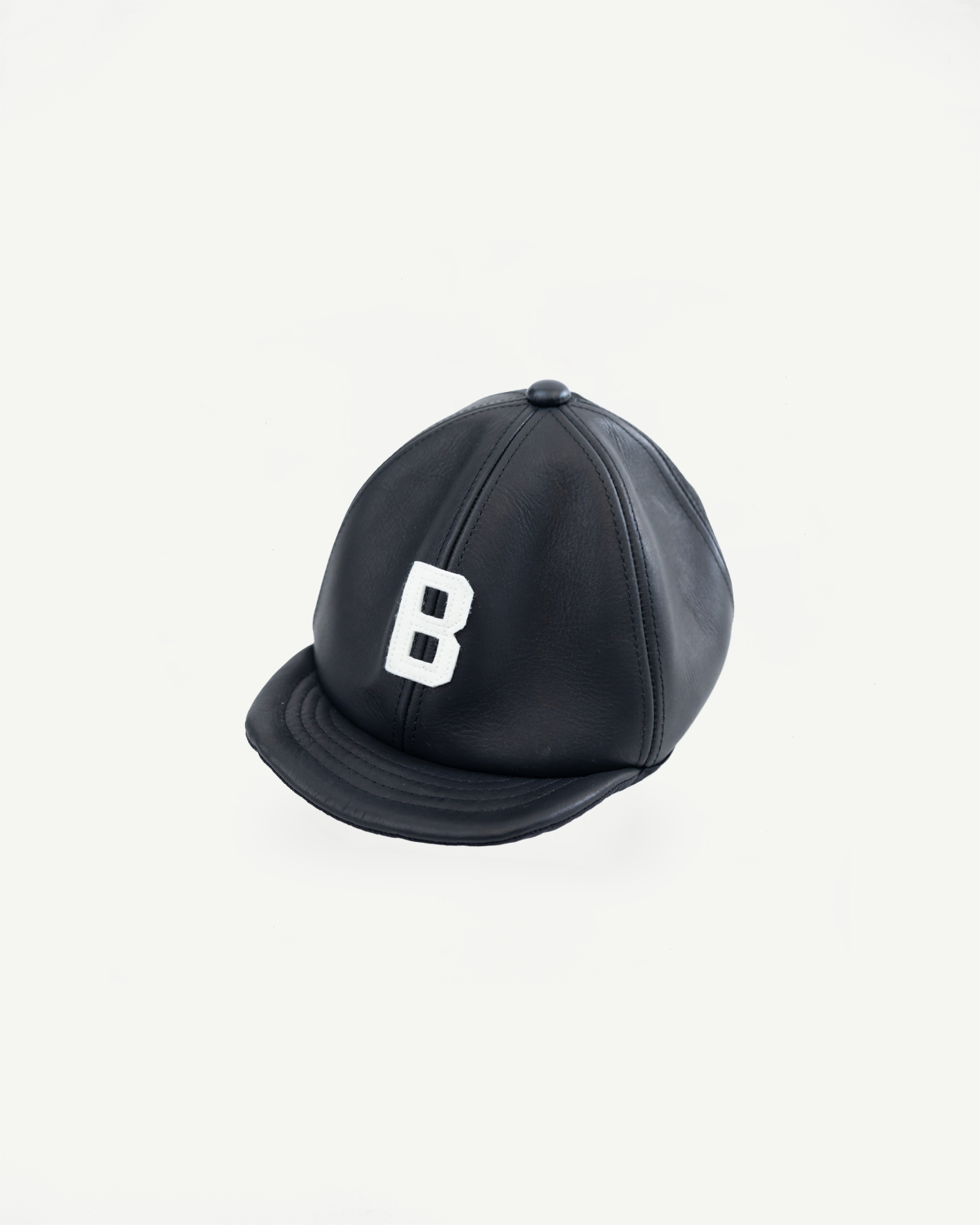 Front flat lay of black leather baseball cap, white B embroidery, curved brim, stitching detail