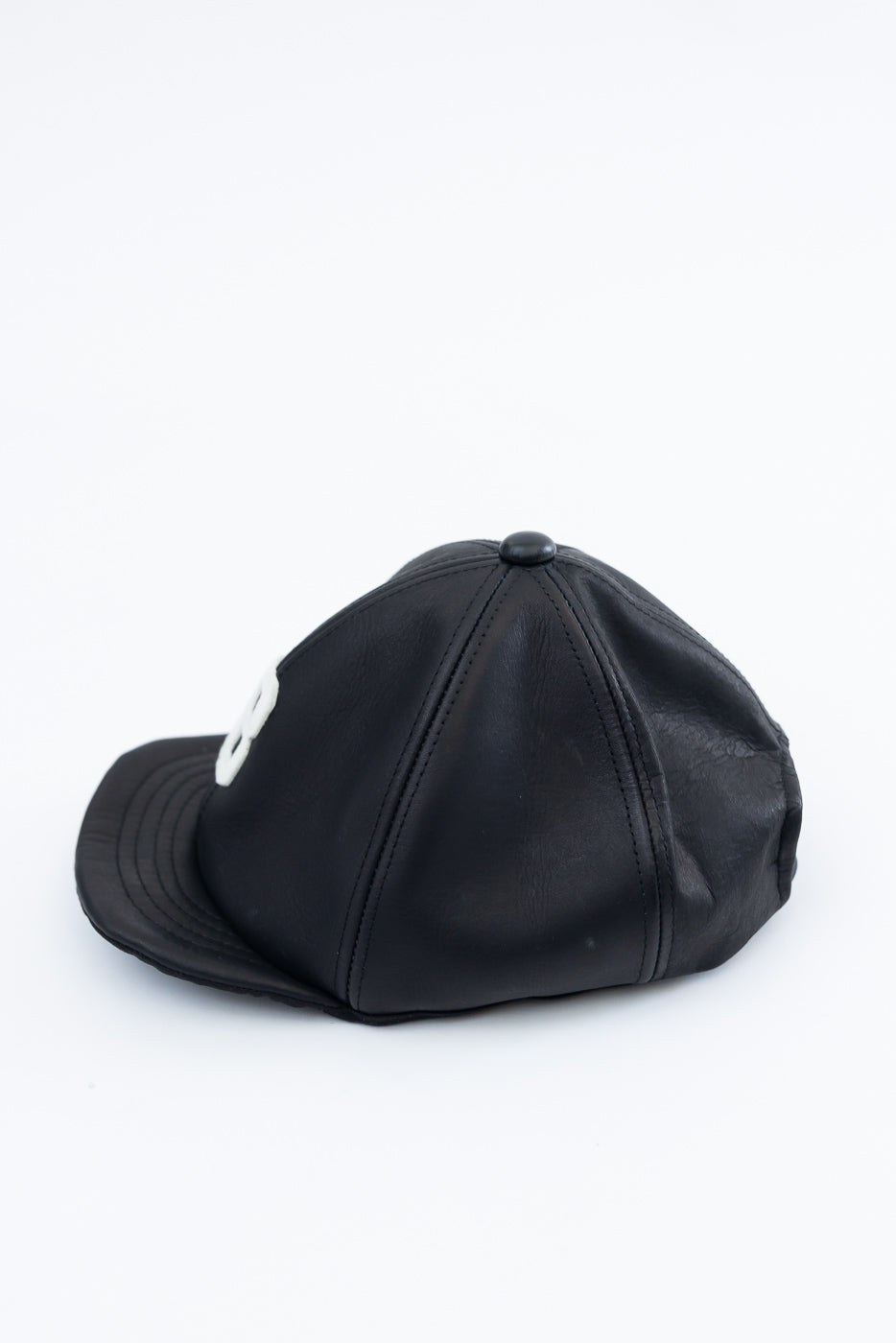 Side view close-up of black leather baseball cap, flat lay, showing brim and side panel stitching.