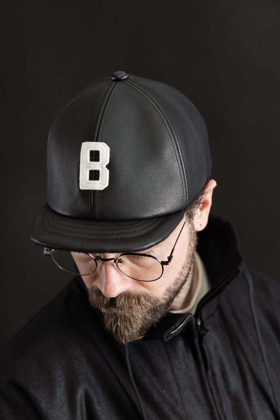 Close-up front view of black leather baseball cap with white letter B, worn by male model, 5'9