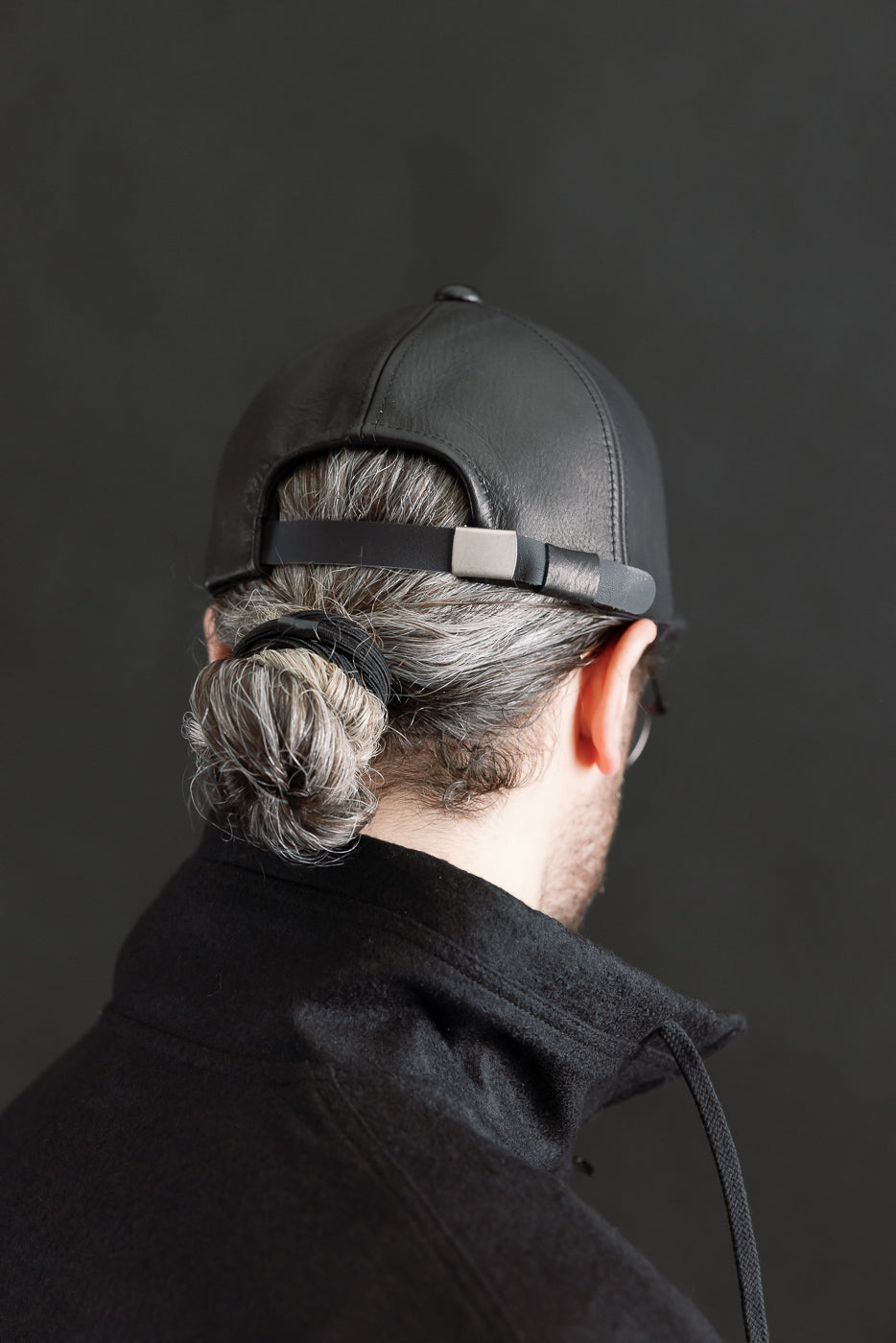 Close-up rear view of black leather baseball cap, adjustable strap, on male model 5'9