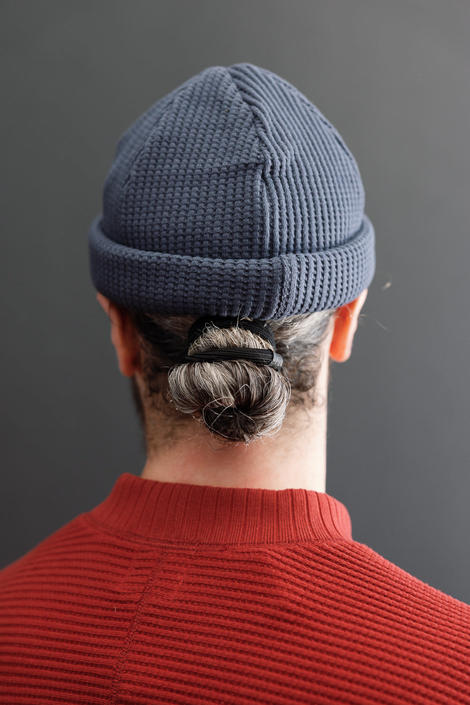 Back view close-up of a navy waffle knit beanie on a male model with hair in a bun.
