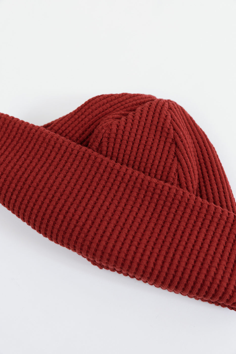 Close-up of a red ribbed knit beanie showing the texture of the folded brim and crown.