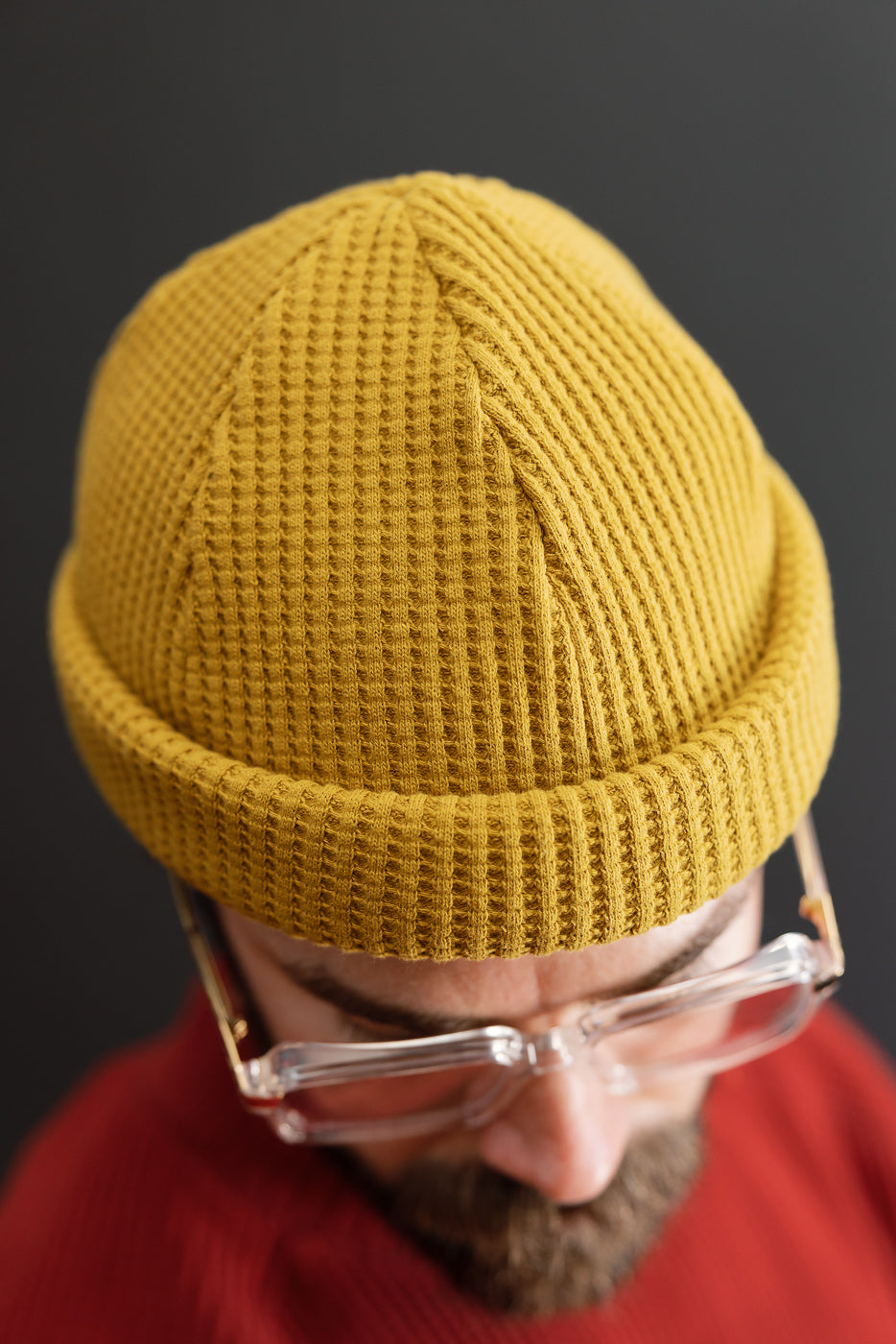 Close-up front view of a mustard yellow waffle-knit beanie on a male model.