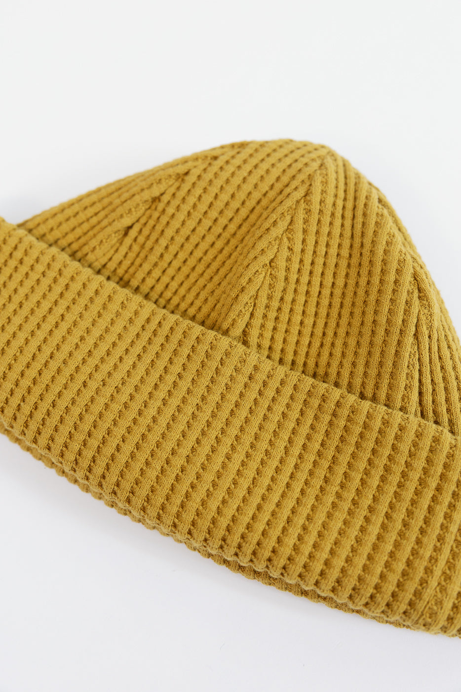 Close-up of the waffle knit fabric texture on a mustard yellow beanie, front view.